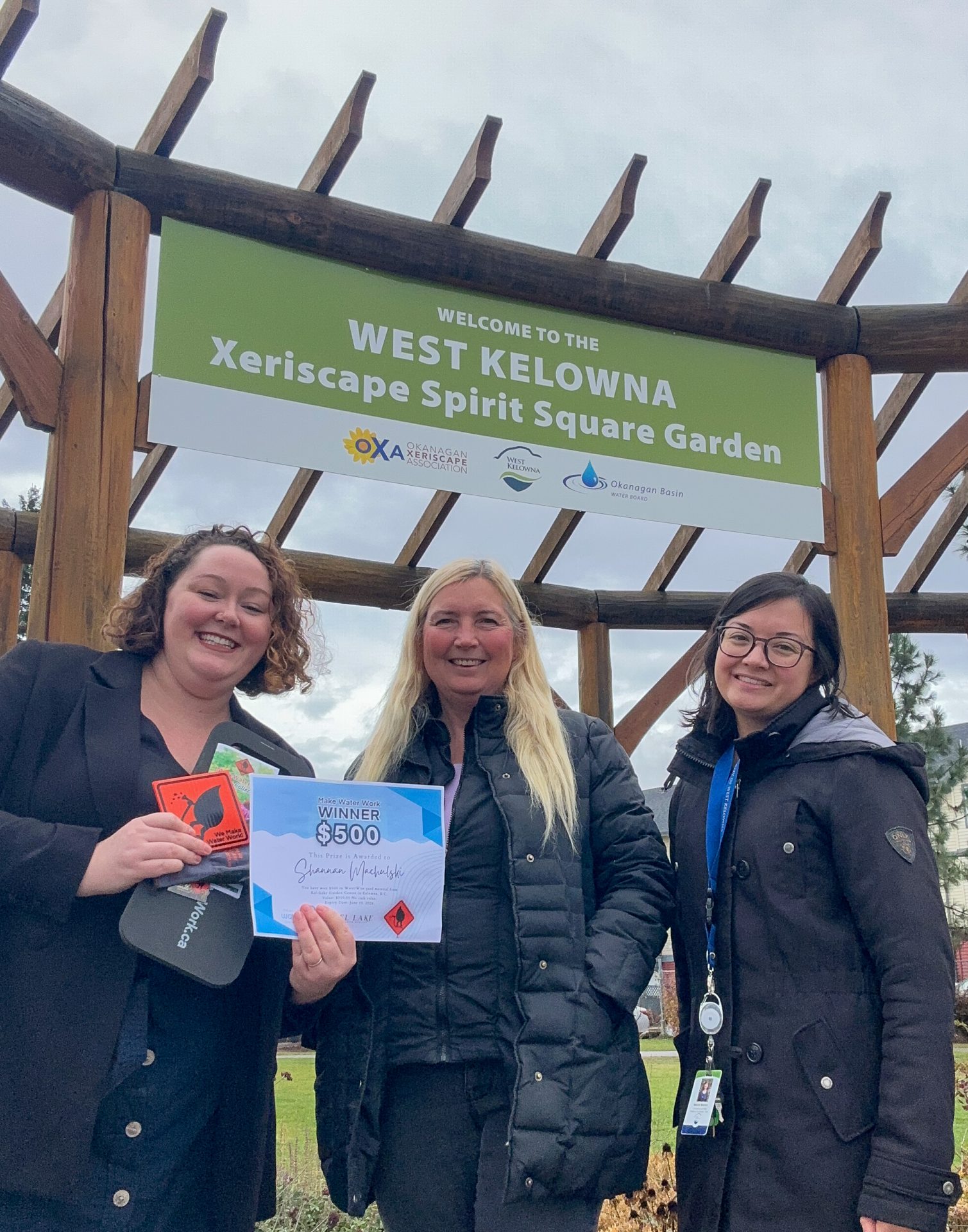 Shannan Machulski (middle) accepts $500 WaterWise yard prize certificate from OBWB Communications Coordinator Amanda Burnett (left) and City of West Kelowna Communications and Engagement Coordinator Melanie Mewhort.